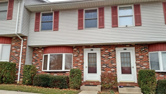 Exterior of townhouse with brick first floor and light gray siding with red shutters on the second floor