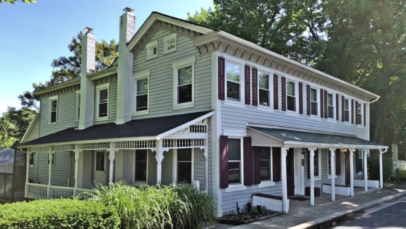 Exterior of duplex with covered front and side porches, light siding, and maroon shutters.