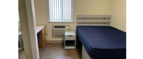 a small room with a bed, desk, and air conditioner