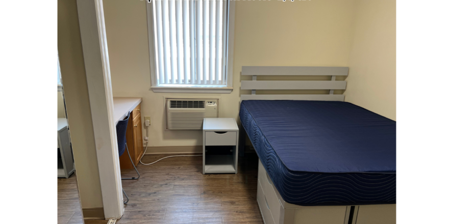 a small room with a bed, desk, and air conditioner