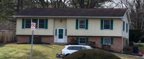 Exterior of house with a shingled roof, white door, emerald green shutters,Light tan siding on the top half and brick on the bottom half