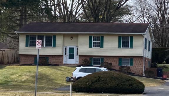 Exterior of house with a shingled roof, white door, emerald green shutters,Light tan siding on the top half and brick on the bottom half