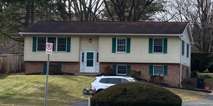 Exterior of house with a shingled roof, white door, emerald green shutters,Light tan siding on the top half and brick on the bottom half