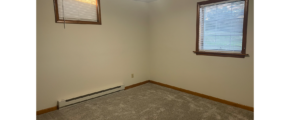 an empty bedroom with gray carpet two windows