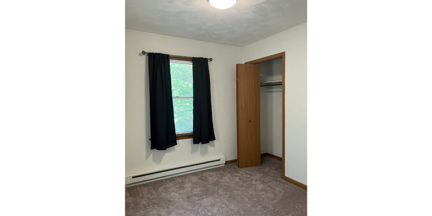an empty room with a closet, carpet, and window