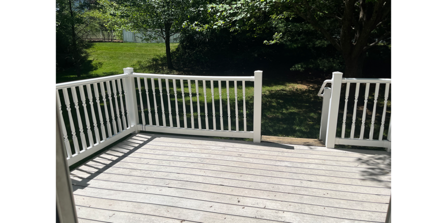 a wooden deck with white railings and trees in the background