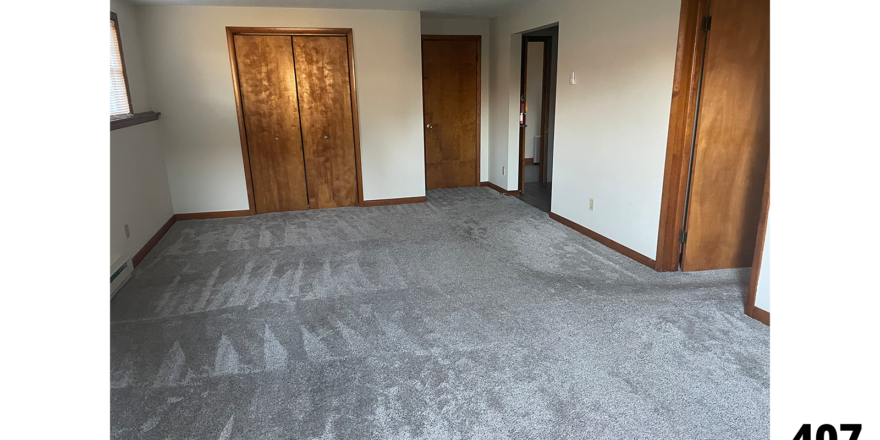 an empty room with gray carpet and wooden doors leading to a closet, washer dryer, and bedroom