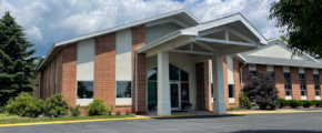 brick church attached to building with glass windows and a parking lot in front of it