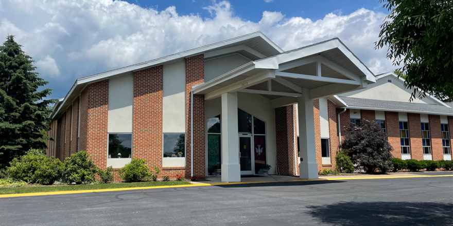 brick church attached to building with glass windows and a parking lot in front of it