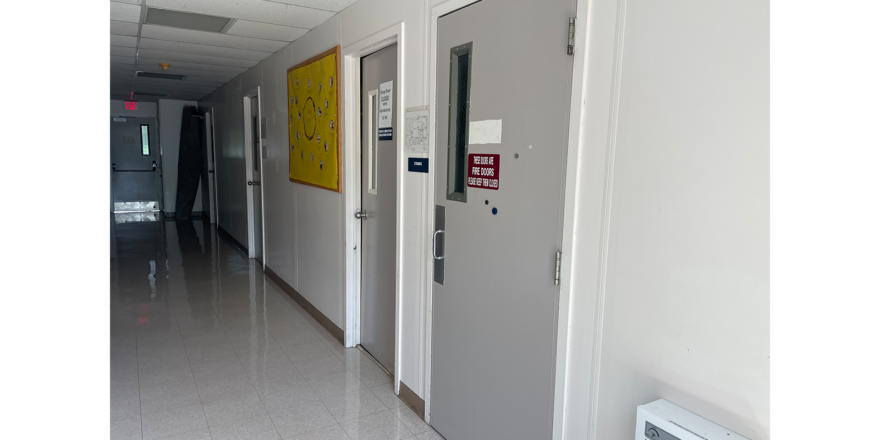 a long hallway with two doors and a yellow sign on the wall