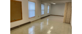 an empty room with 3 windows, white walls, overhang lights, and white tile