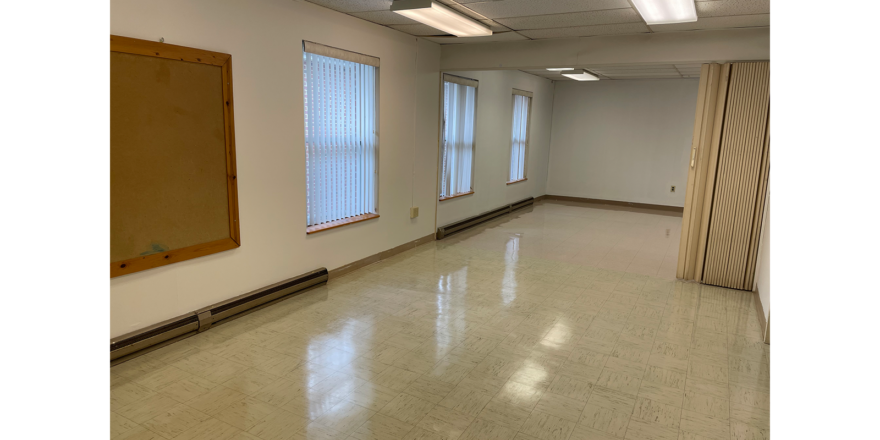 an empty room with 3 windows, white walls, overhang lights, and white tile