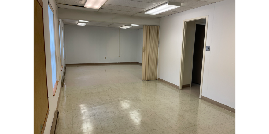 an empty room with 3 windows, white walls, overhang lights, and white tile