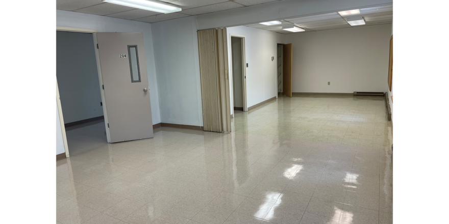 an empty room with 3 doorways , white walls, overhang lights, and white tile