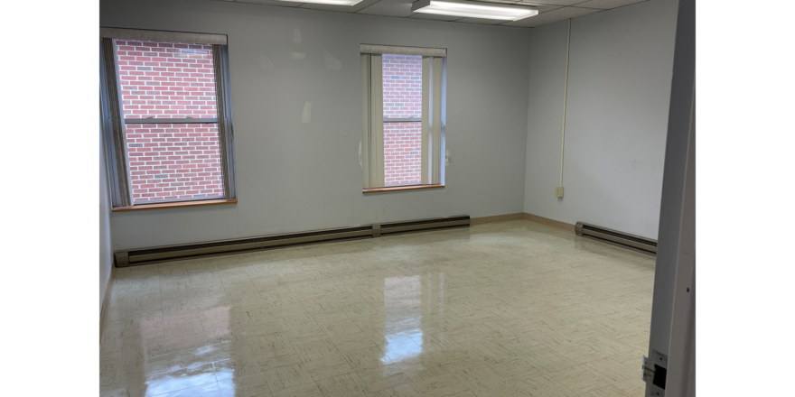 an empty room with 3 windows, white walls, overhang lights, and white tile