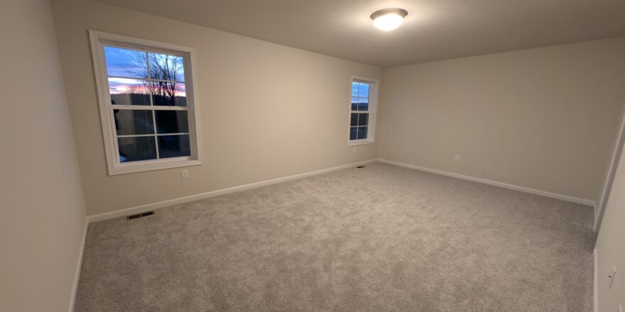 an empty room with carpet and two windows